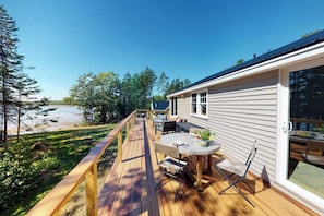 Eine Terrasse mit Gartenmöbeln, einem Tisch und Stühlen mit Blick auf Strand und Wald.