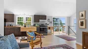 A spacious living area with a sofa, a wooden chair, a dining table, and a kitchen with a view.