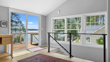 A room with a view of a lake, a wooden desk, a patterned rug, and a staircase with a railing.