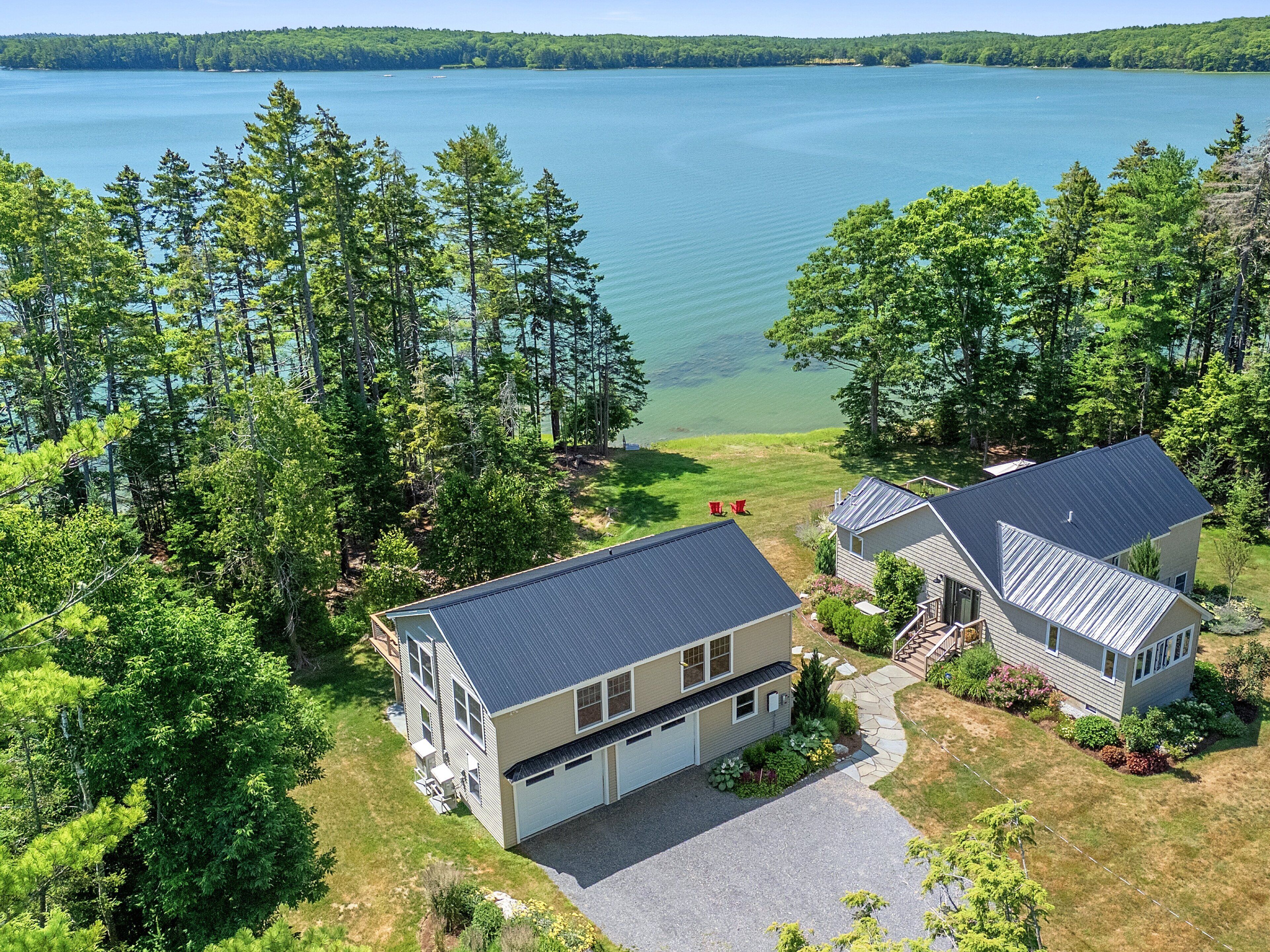 A two-story house with a garage, surrounded by a well-maintained lawn and trees, near a large body of water.