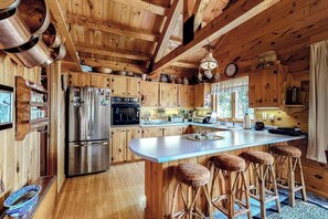 Cocina de cabaña de madera con una isla grande, taburetes de bar, un refrigerador y una estufa.