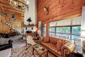 L’intérieur d’une cabane en rondins, avec une cheminée, un canapé en cuir et un escalier menant à une terrasse.