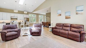 A spacious living room with a brown leather sofa, two armchairs, and a dining area with a white table and chairs. - Newly Renovated Home w/ Large Yard & Great Kitchen - Near Downtown & Acadia (Bar Harbor)