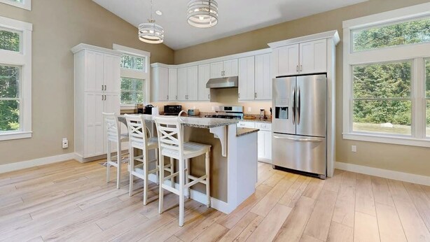 A kitchen with white cabinets, a stainless steel refrigerator, a central island with bar stools, and pendant lighting. - Newly Renovated Home w/ Large Yard & Great Kitchen - Near Downtown & Acadia (Bar Harbor)