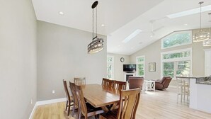 A spacious dining area with a wooden table and chairs, a hanging light fixture, and large windows allowing natural light. - Newly Renovated Home w/ Large Yard & Great Kitchen - Near Downtown & Acadia (Bar Harbor)