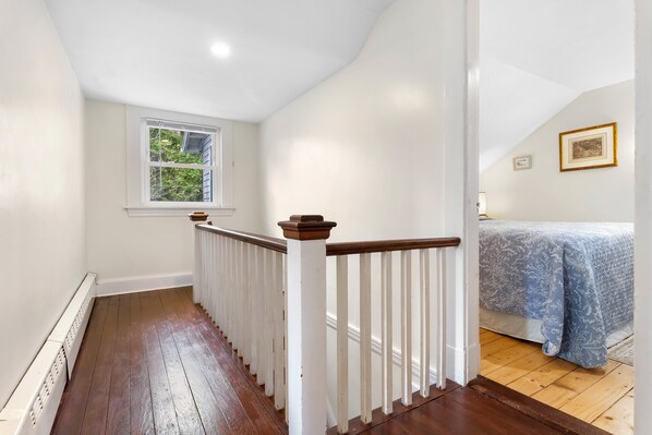 A staircase with white railings and a wooden floor leading to a bedroom with a bed and a window. - Bright, Spacious Getaway With Full Kitchen, Furnished Porch & Wifi - Near Trails (Seal Harbor)