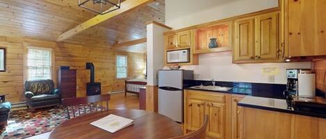 A wooden cabin interior with a dining table, kitchen area, and a fireplace.