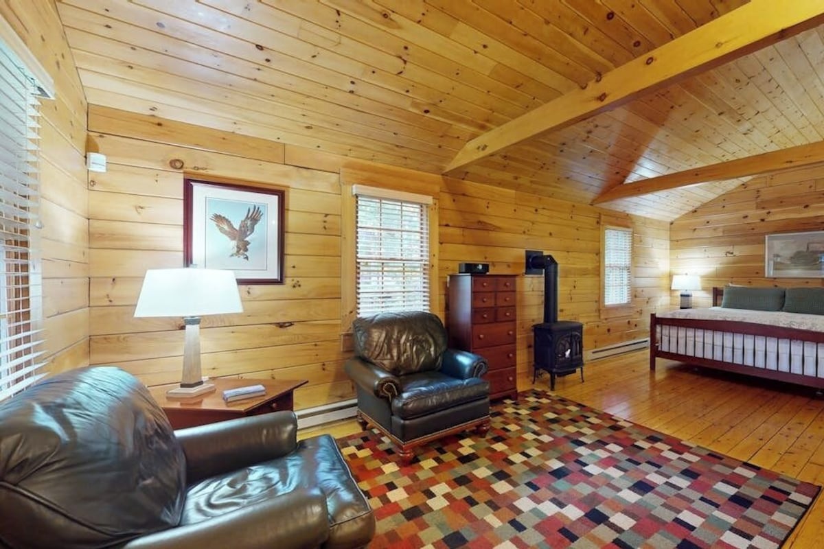 A log cabin interior with a fireplace, leather furniture, and a patterned rug.