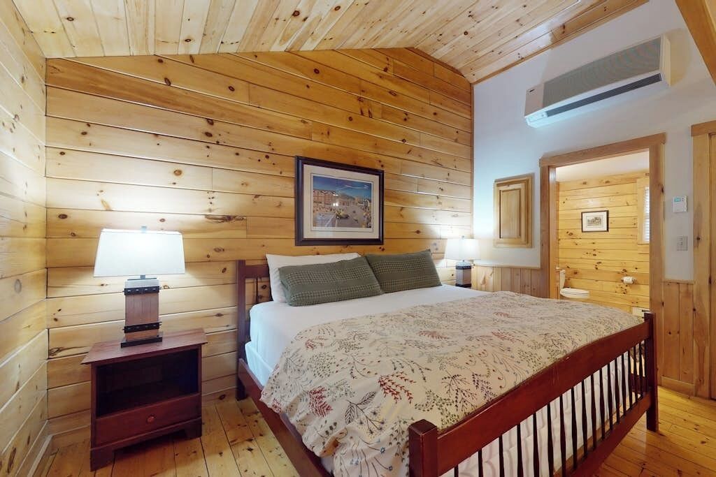 Une chambre aux murs lambrissés, avec un lit, des tables de chevet et un tableau encadré accroché au mur.