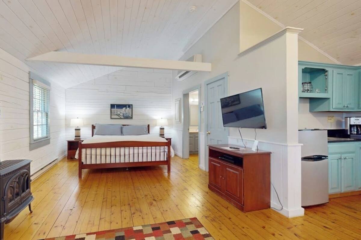 Un dormitorio con cama de madera, televisión, zona de cocina con armarios color turquesa y chimenea.