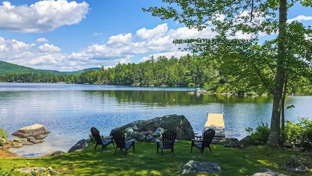 A lakeside setting with outdoor seating and a dock. - Spacious Lakefront Home With a Sandy Beach, Kayaks, and Stunning Panoramic Views (Holden)