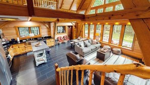 A spacious wooden cabin with a kitchen, dining area, and living room, featuring large windows and a wooden staircase.