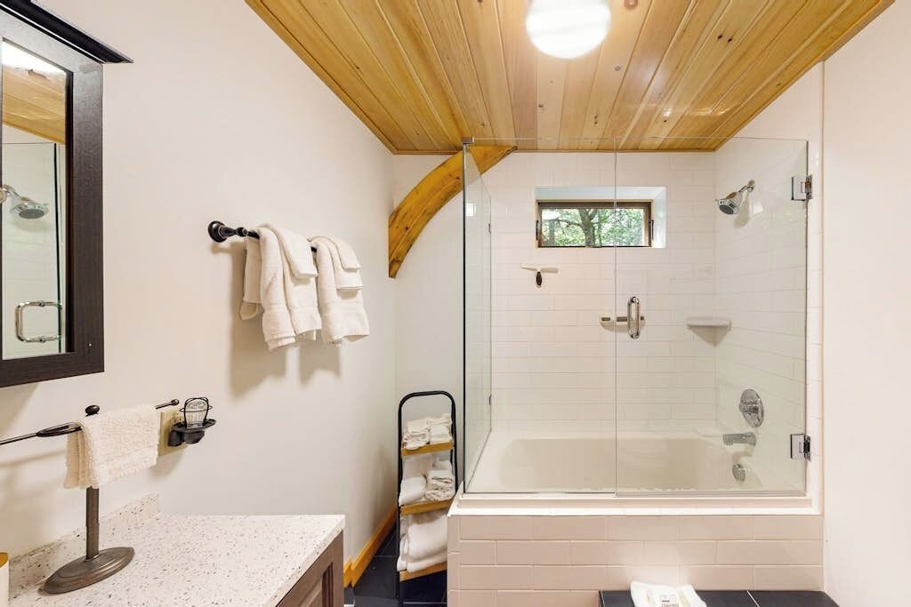 A modern bathroom with a glass-enclosed shower, a large mirror, and a wooden ceiling.