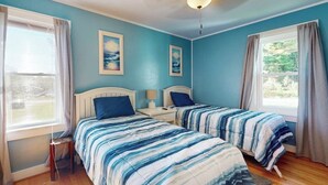 Un dormitorio con dos camas, un ventilador de techo y dos ventanas con cortinas.