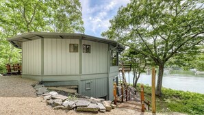 Eine kleine, hellfarbene Holzhütte mit Veranda und einem Steinweg, der darauf führt.