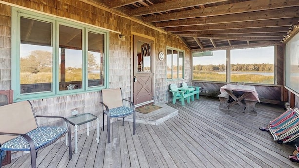 Une véranda couverte avec un plancher en bois, une table, des chaises et une vue sur l’extérieur.