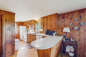 A kitchen with wooden cabinets, a white countertop, a microwave, a sink, and a small table with a lamp.