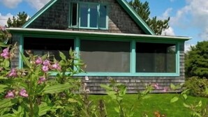 Une maison avec un toit à pignon, une véranda aux boiseries vertes et un garage.