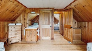 Un intérieur en bois avec une porte centrale, une commode et un lit à l’arrière-plan.