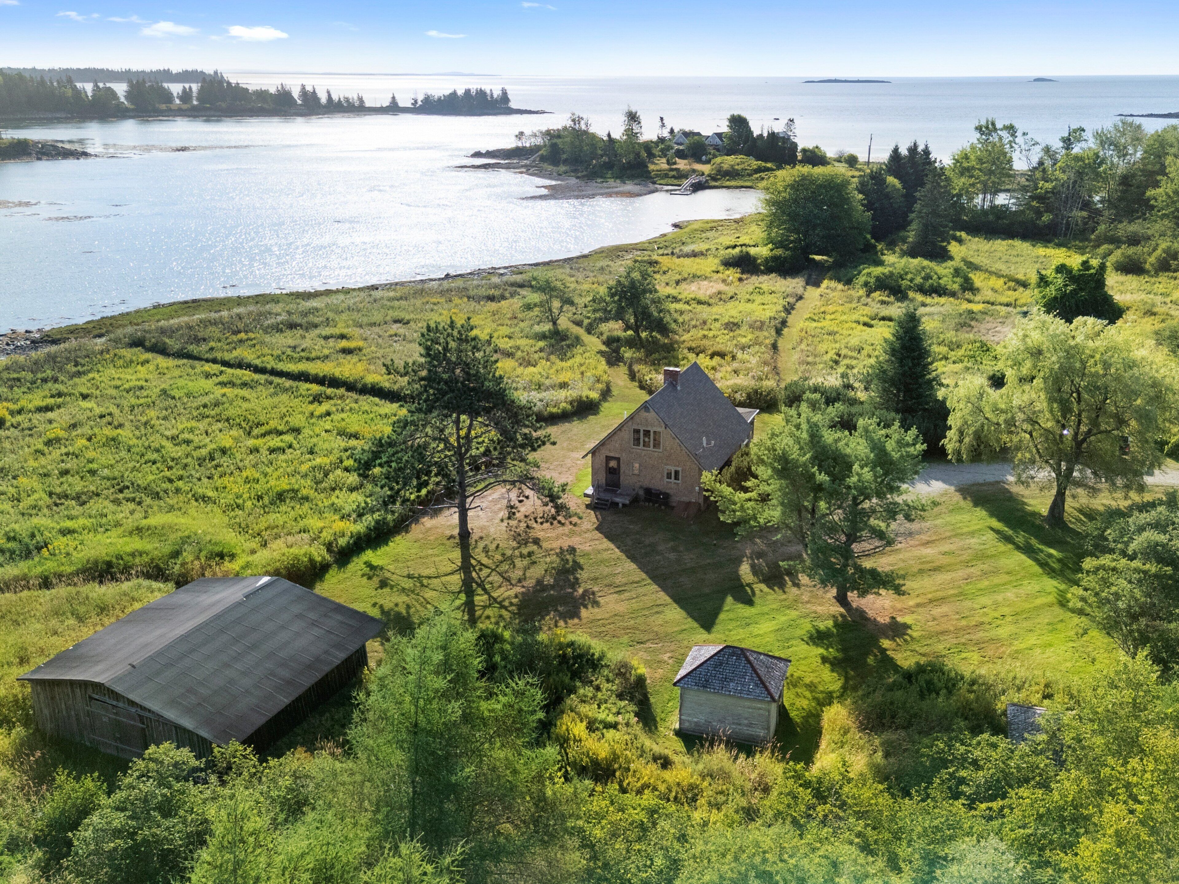 A rural property with a house, a barn, and a small shed, surrounded by lush greenery and a body of water.