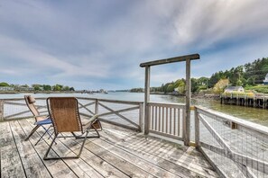 Eine Holzterrasse mit einem Holzstuhl und einem kleinen Tisch, mit Blick auf ein Gewässer und einem Steg im Hintergrund.
