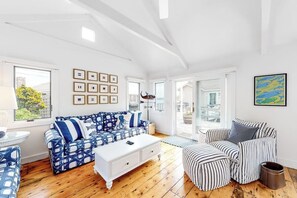 A spacious living room with a patterned sofa, a white coffee table, and striped ottomans. - Oceanfront Cottage & Studio on Mill Cove w/ Water Views, Deck - Walk Downtown (Boothbay Harbor)