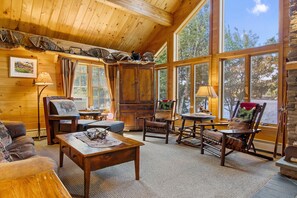 A cozy cabin interior with wooden walls, large windows, a fireplace, and rustic furniture. - Lakeside Lodge With Amazing Water Views, Screened Porch, Dock, & Firepit (Greenville)