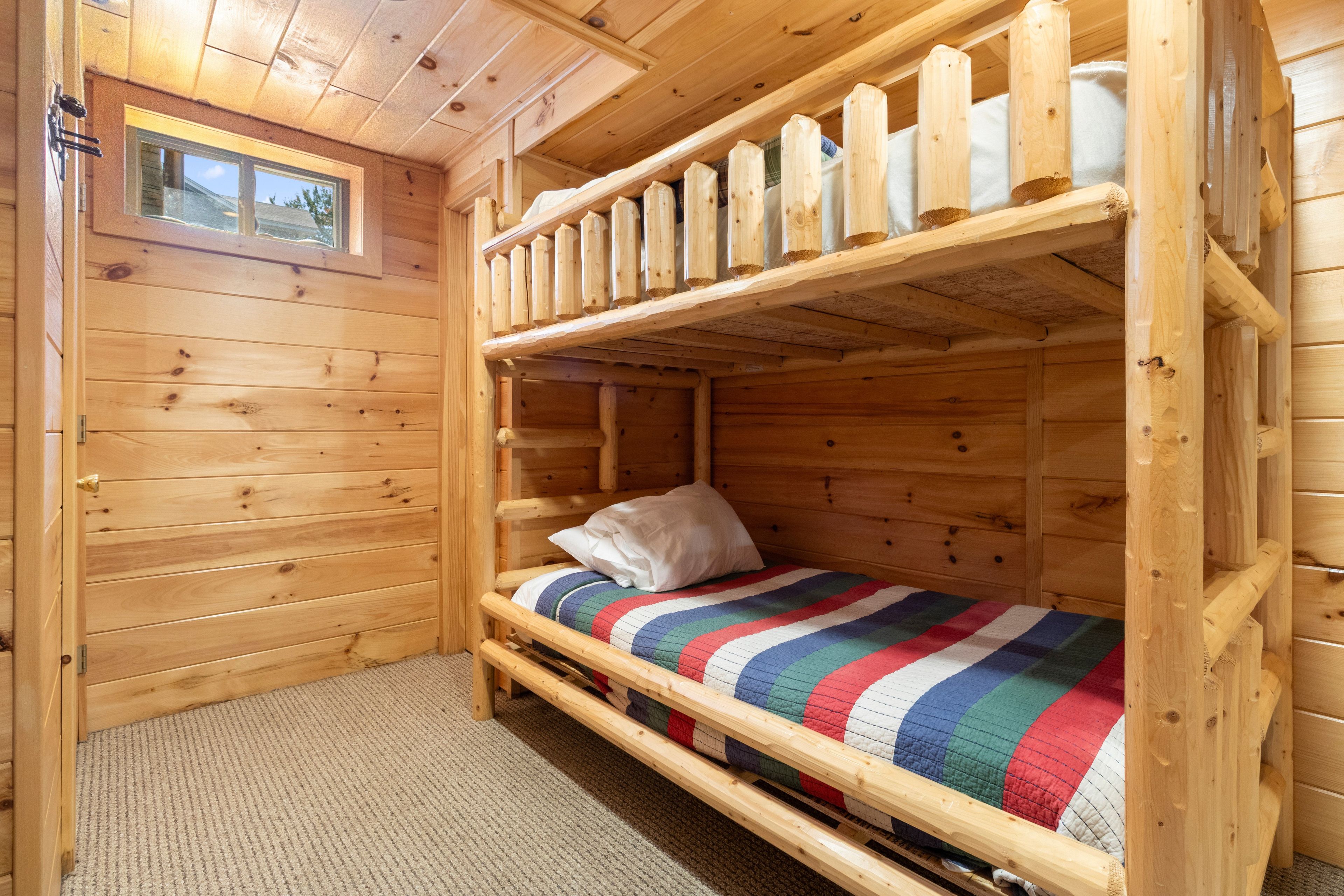 A wooden cabin room with a bunk bed, a window, and a view of the outdoors.
