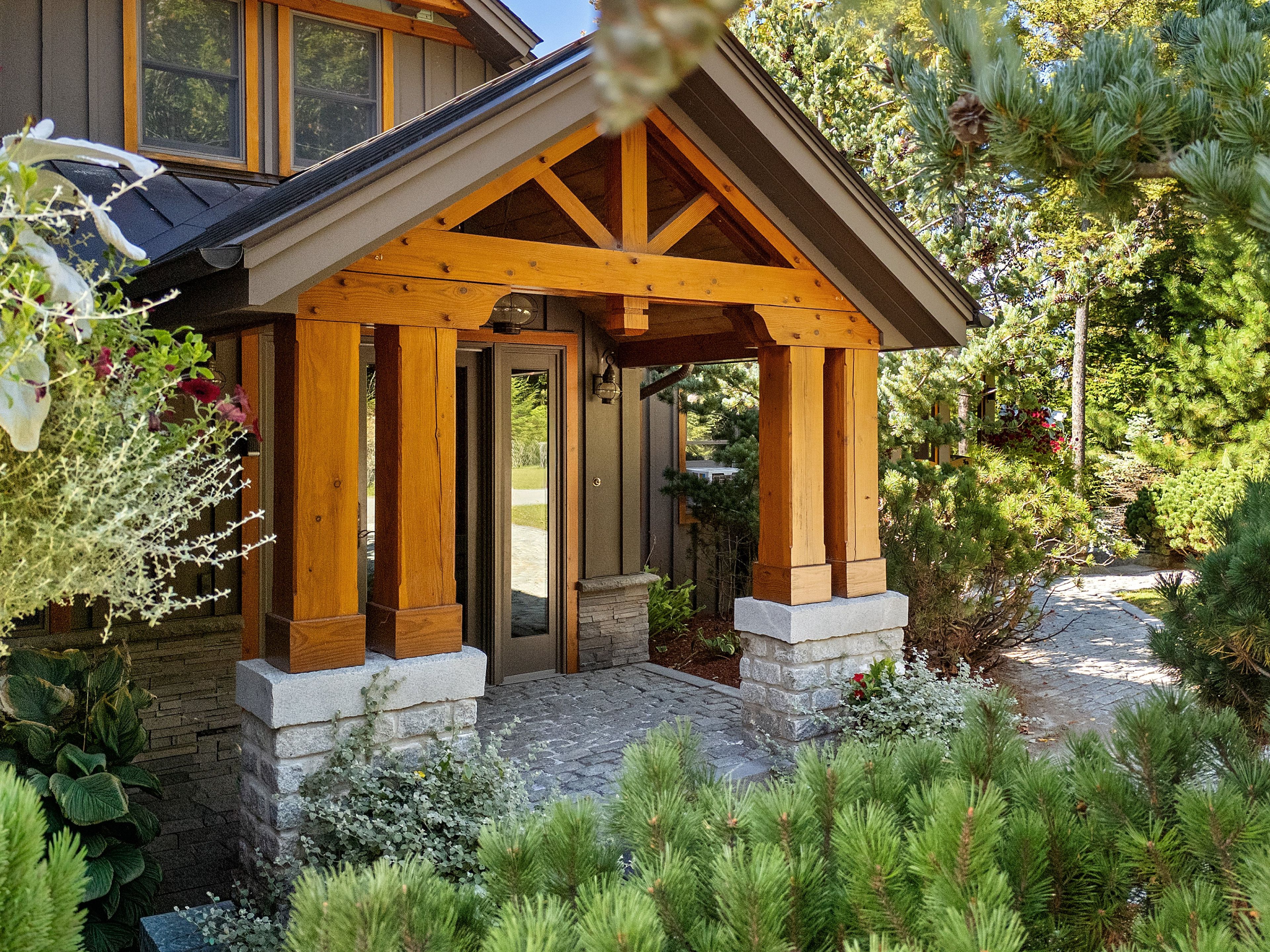 A wooden house with a stone foundation, a covered porch, and a garden with various plants.