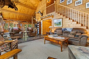 Un interior espacioso de madera con techo alto, chimenea, escalera y un rincón de estar acogedor.