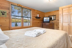 A wooden cabin room with a bed, a television, and a window overlooking a lake. - Lakeside Lodge With Amazing Water Views, Screened Porch, Dock, & Firepit (Greenville)