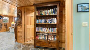 A wooden bookshelf filled with books in a room with wooden walls and a stone-tiled floor.