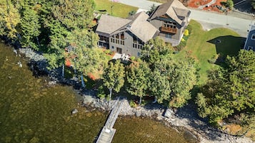 An aerial view of a house with a dock extending into a body of water, surrounded by dense trees.