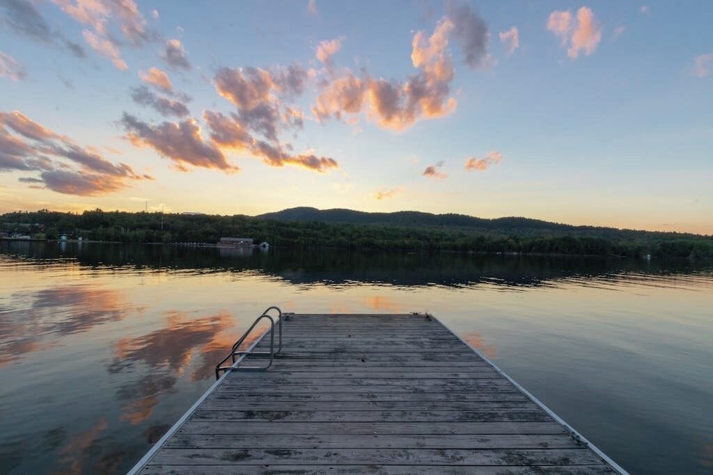 A wooden dock extending into calm water with a sunset sky.