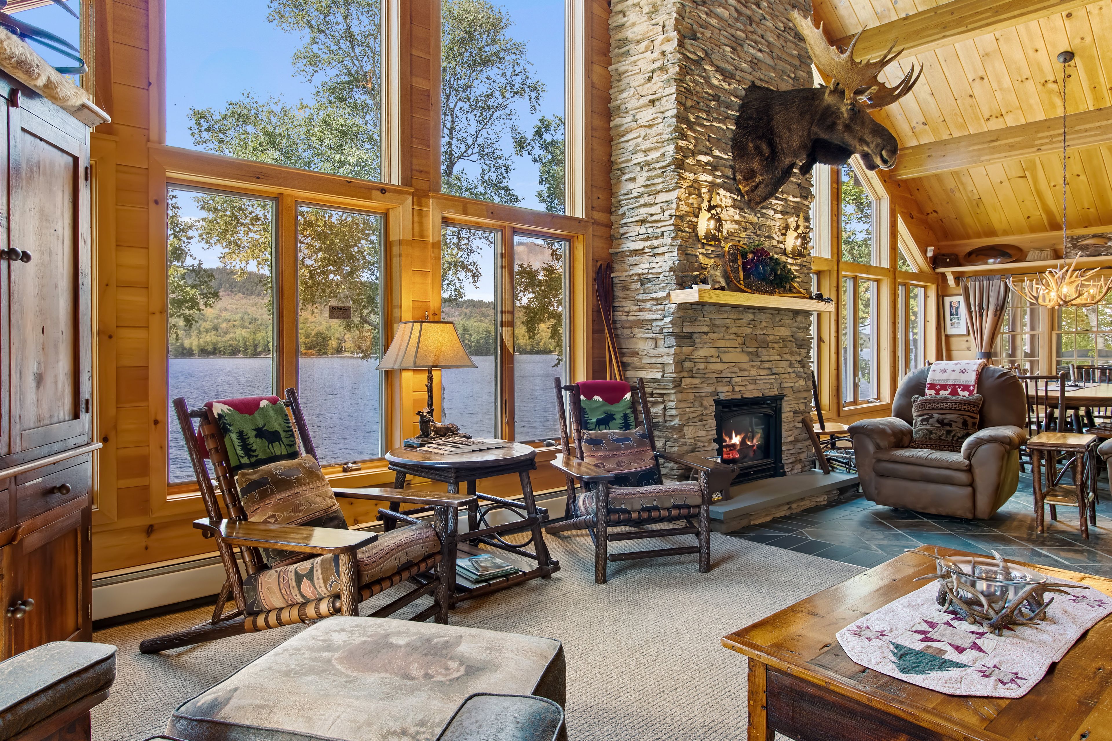 L’intérieur chaleureux du chalet est agrémenté d’une cheminée en pierre, de meubles en bois et de grandes fenêtres qui offrent une vue sur le paysage extérieur.