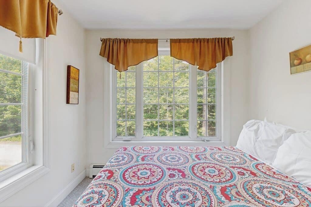 Un dormitorio con un ventanal grande, una colcha estampada y vistas a árboles.
