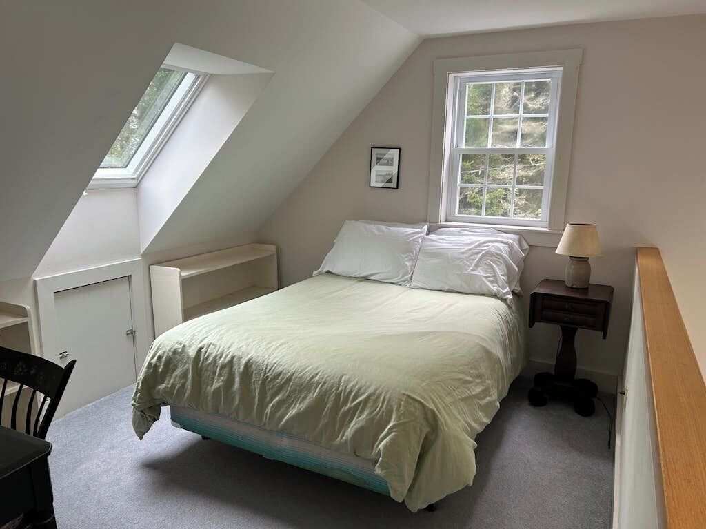 Une chambre avec un plafond en pente, un lit, une fenêtre, un bureau et une chaise.