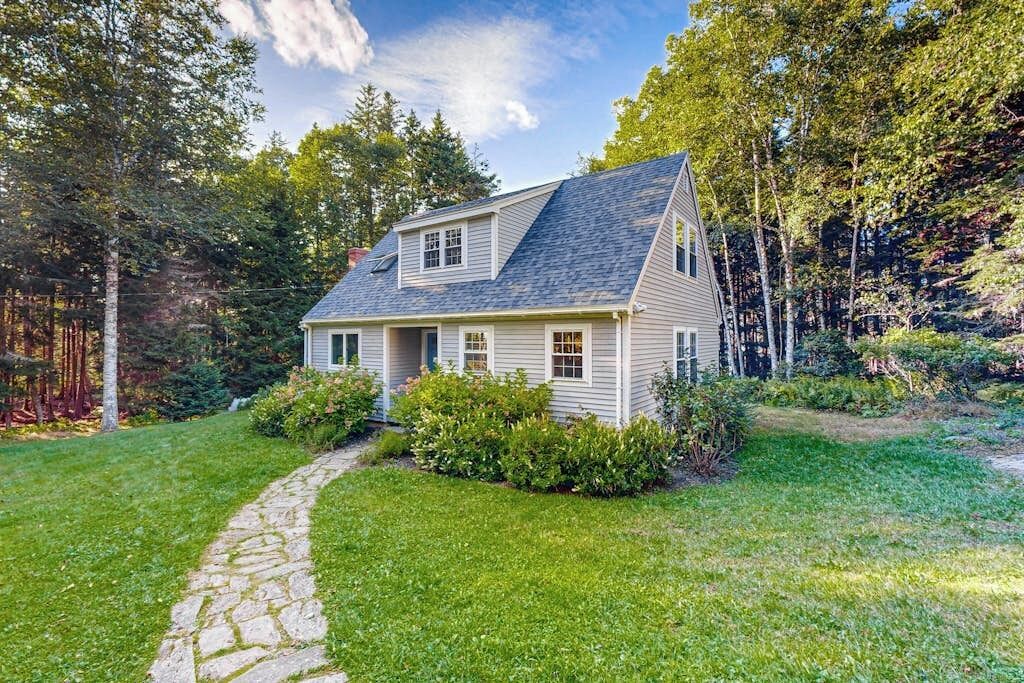 A two-story house with a stone pathway leading to the front door, surrounded by lush greenery and trees.