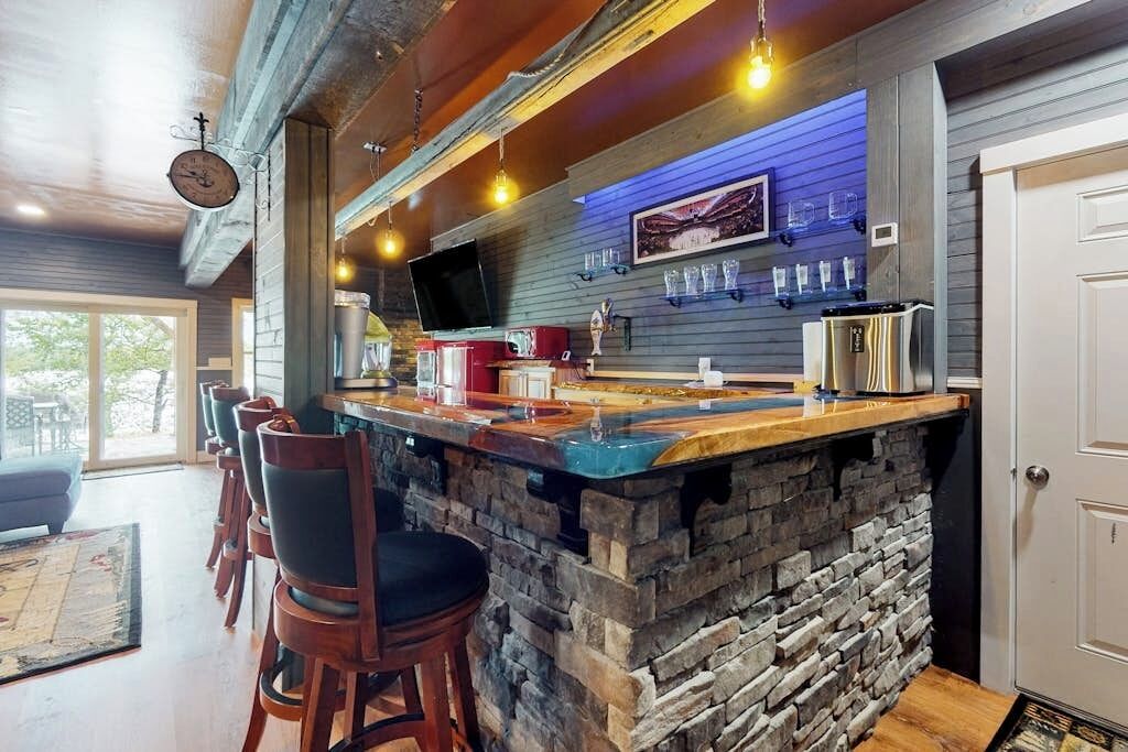 A bar area with a stone counter, bar stools, a television, and a wall-mounted wine rack.