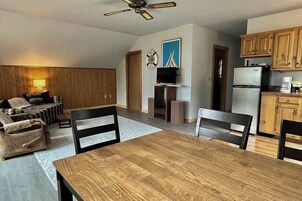 Un comedor con una mesa y sillas de madera, una televisión y una cocina con armarios de madera.