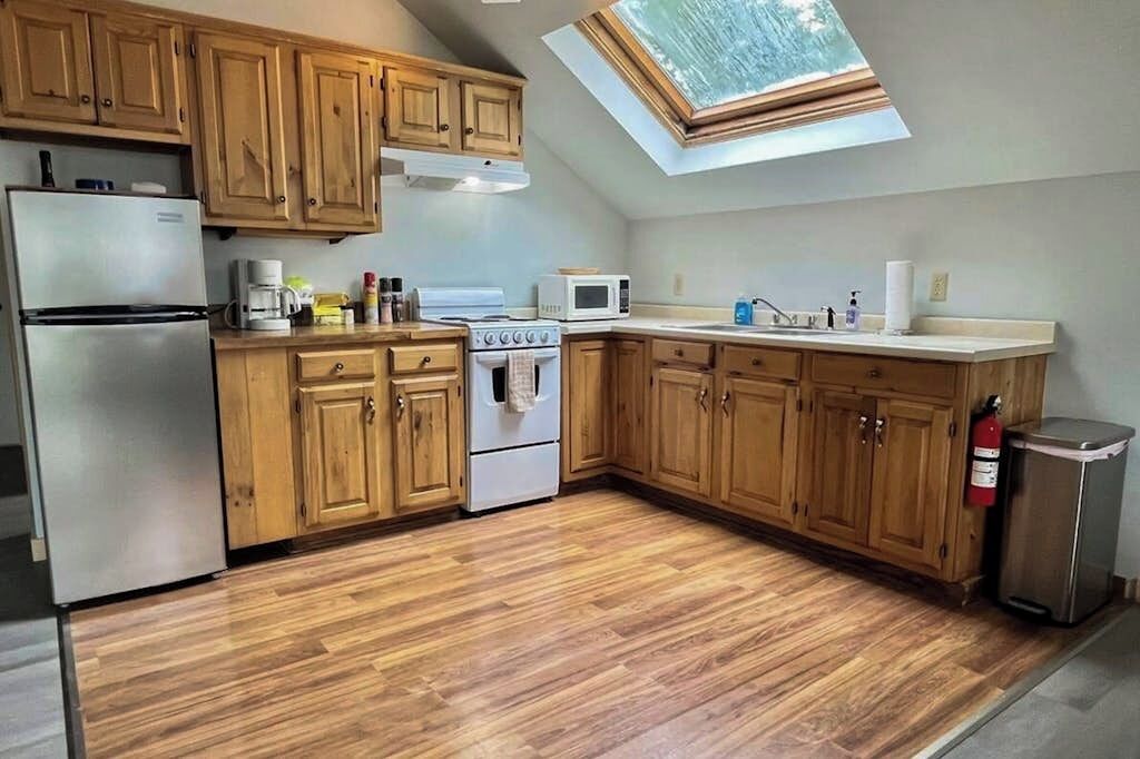 A kitchen with wooden cabinets, a stainless steel refrigerator, a stove, a microwave, and a skylight.