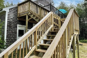A wooden staircase leading to a deck with a black railing and a blue umbrella. - Charming Apartment With Ocean Views, Private Deck, and Easy bay Access (Trenton)