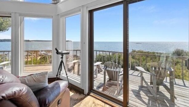 A room with a large sliding glass door leading to an outdoor deck with chairs and a view of the water. - Clark Point Cottage, Ocean Access, Panoramic Views (Spruce Head)