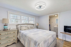 A bedroom with a bed, dresser, lamp, TV, and a window. - Coastal Bungalow With Large Yard, Beautiful Kitchen, & Great Location (Boothbay Harbor)