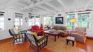 A spacious living room with wooden floors, a large window, and a high ceiling with exposed beams. - Waterfront Dog-friendly Cottage With Amazing Views, Deck, Grill, & Washer/dryer (Cushing)