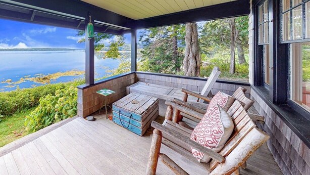 A covered porch with a wooden bench, a small table, and a view of a lake. - Waterfront Dog-friendly Cottage With Amazing Views, Deck, Grill, & Washer/dryer (Cushing)