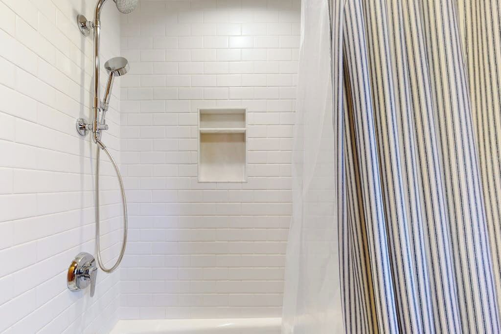 A shower with a handheld showerhead, a wall-mounted faucet, and a rectangular shelf.