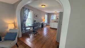 A dining area with a table and chairs, a kitchen with cabinets, and an arched doorway.