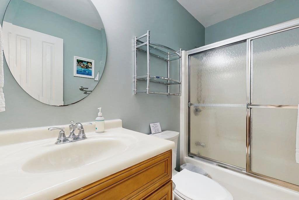 A bathroom with a white sink, a mirror, a shower enclosure, and a towel rack.