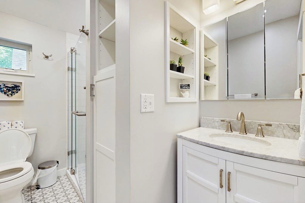 A bathroom with a toilet, shower, and vanity with a sink and mirror.